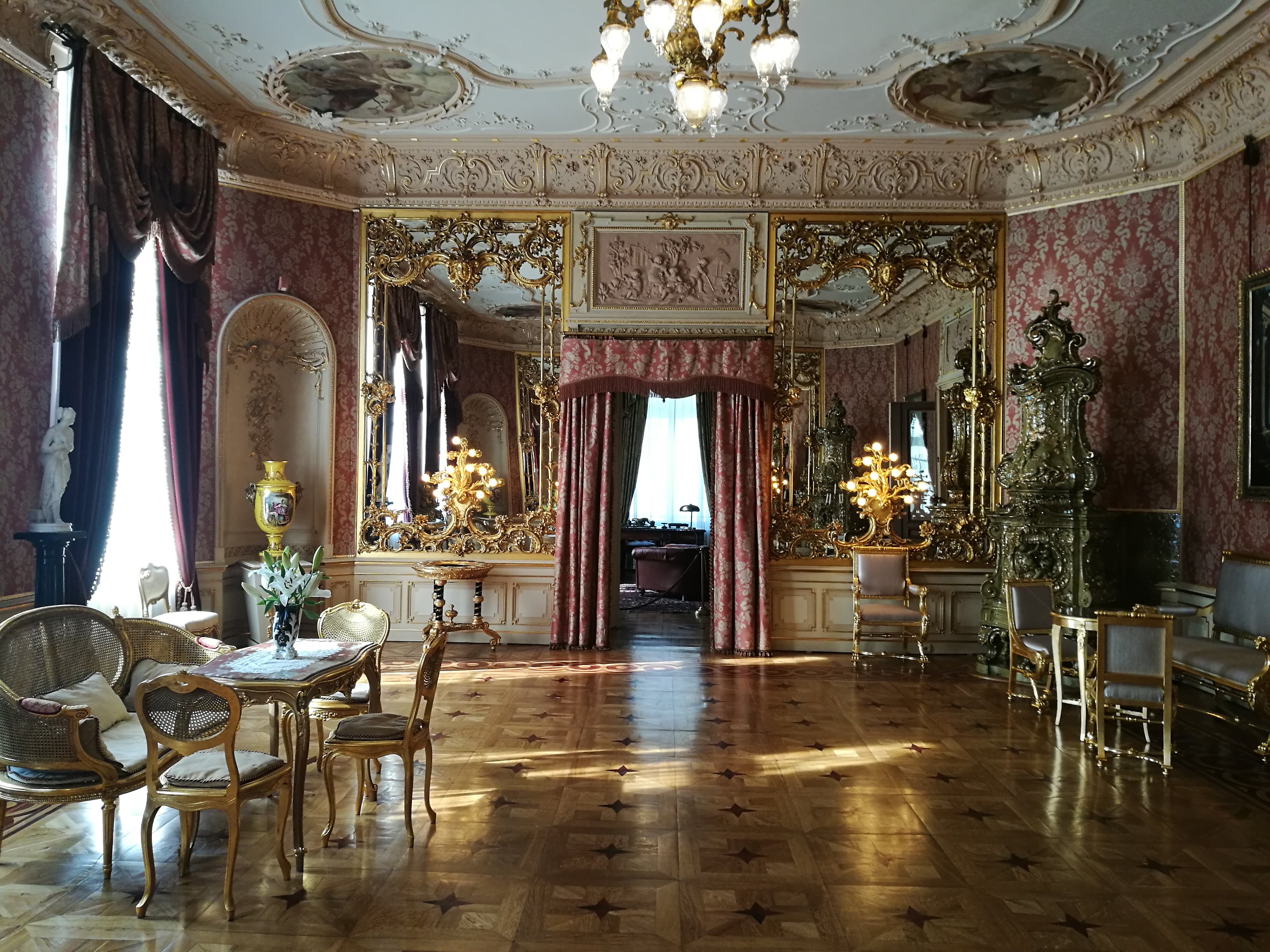 A room with gilded furniture, walls, ceiling. At the far end is a doorway surrounded by pink curtains.