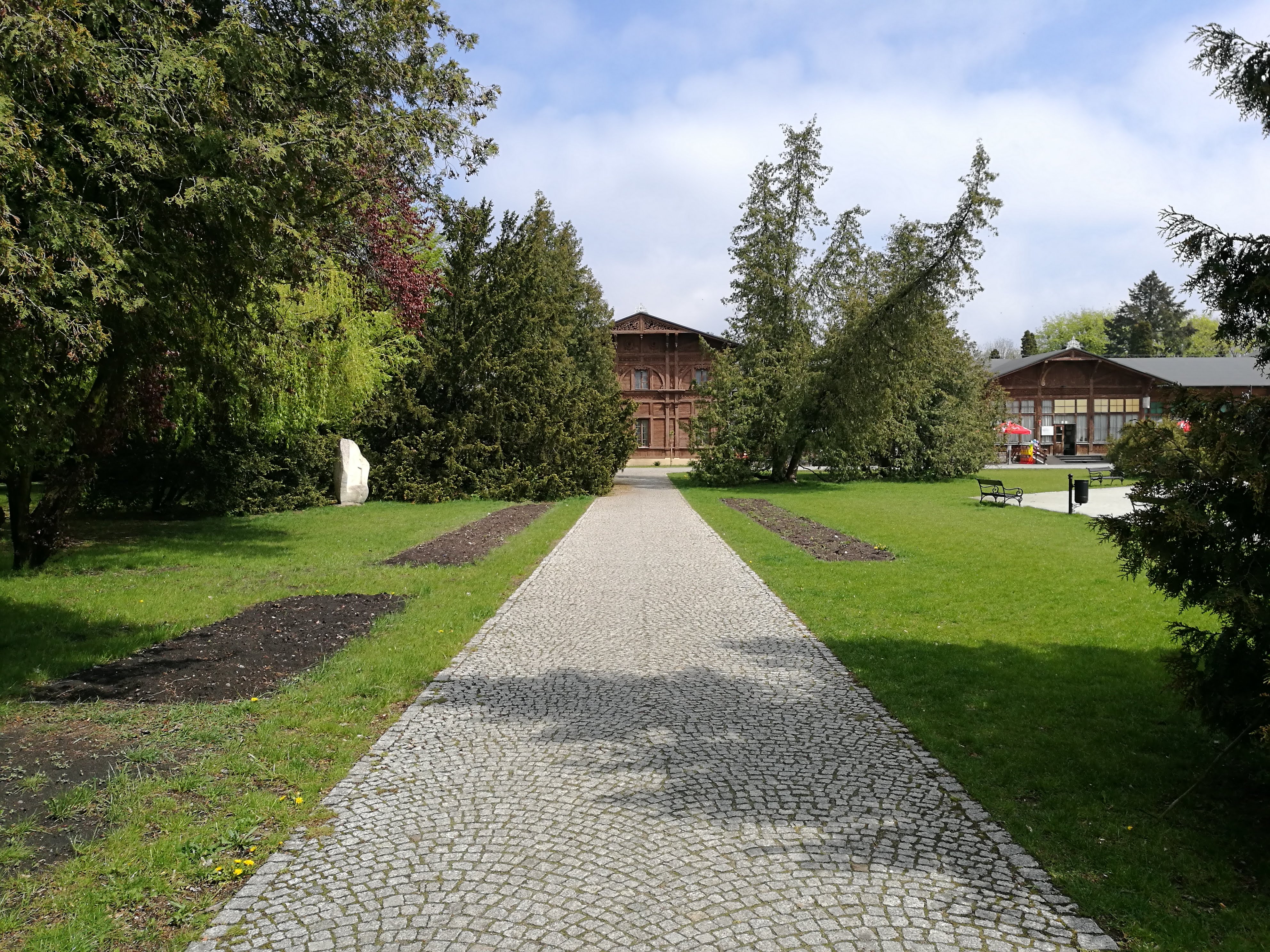 A path made up of small square grey bricks, leading to a wooden building in the distance.