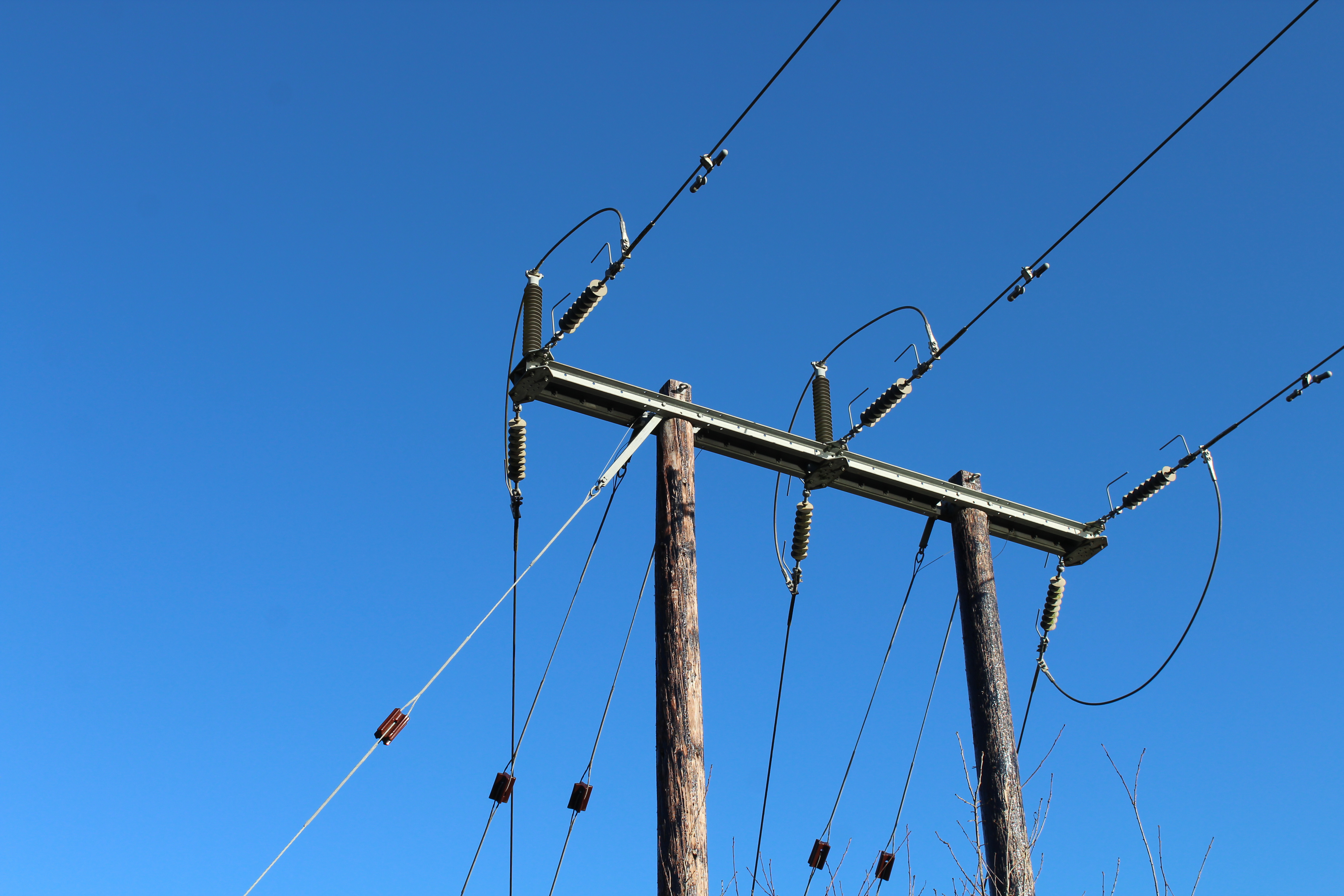 Three power lines come together at a terminal, the wooden beams rising out from the bottom of the picture.